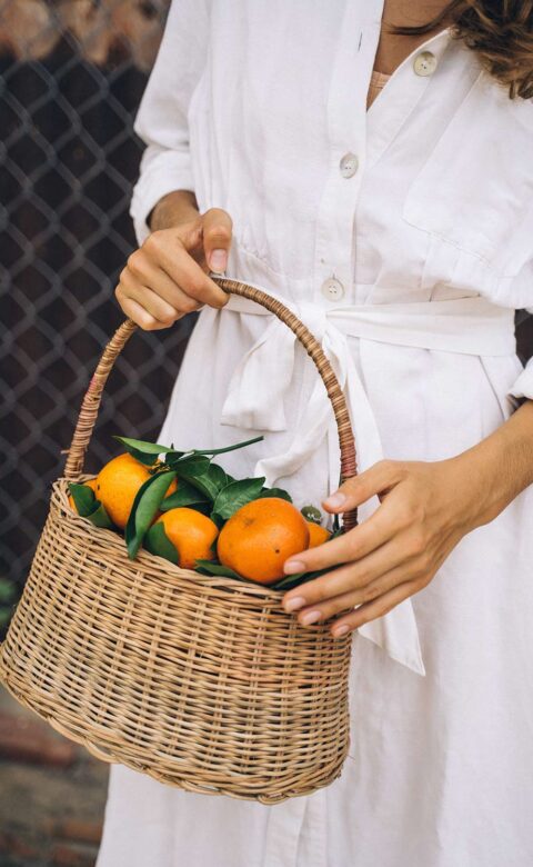 Woman holding wicker basket full of tangerines